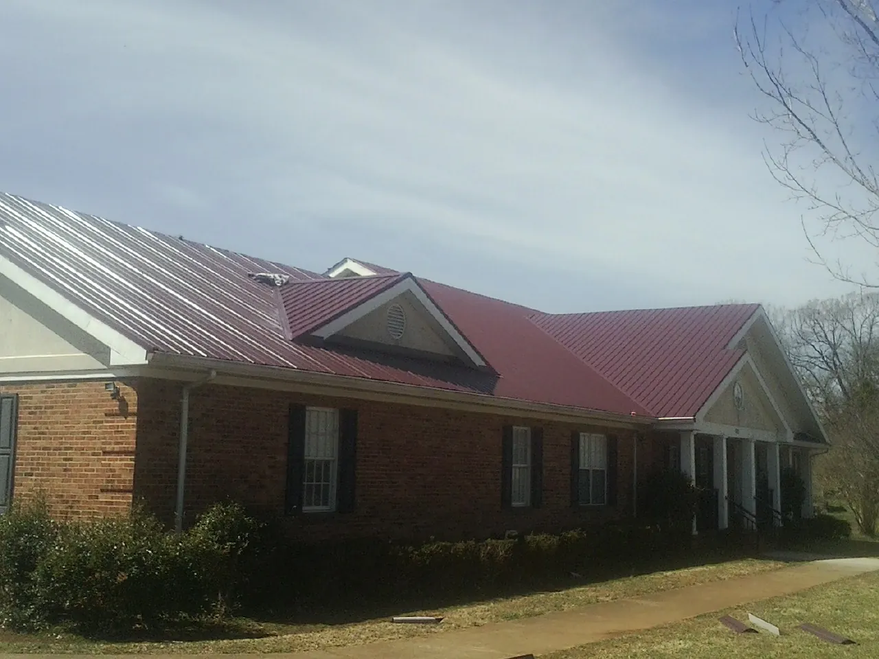 Red metal roof with gabled entries on a long brick building, from a Hail Damage Roof Repair job in Fairplay