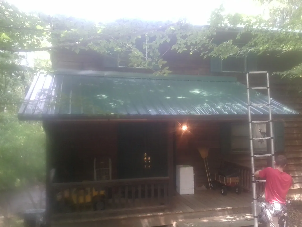 Worker on a ladder at the green porch roof of a wooded cabin in Fairplay
