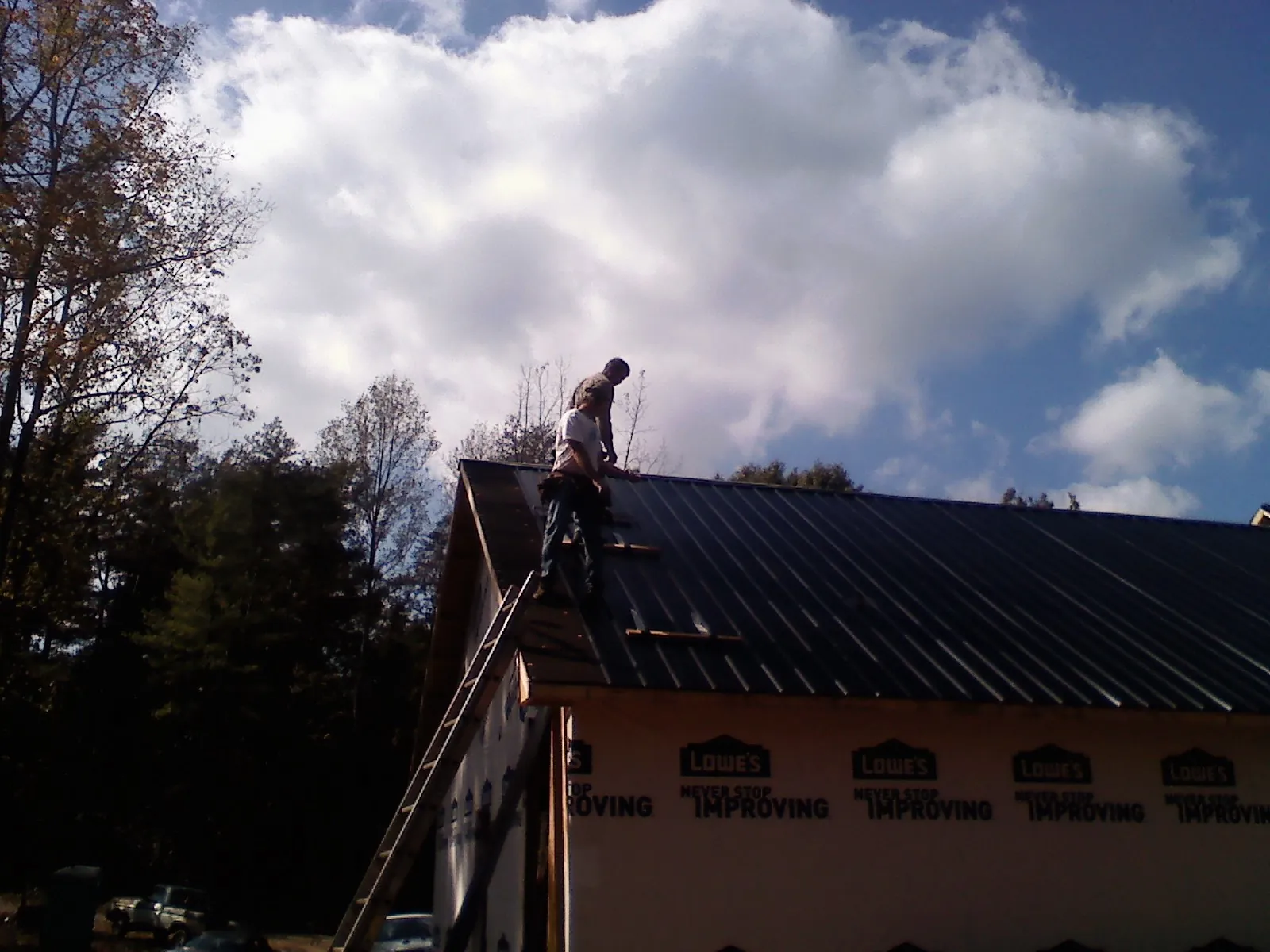 Roofer fastening dark metal panels high against a cloudy sky, from a Roof Inspection job in Fairplay