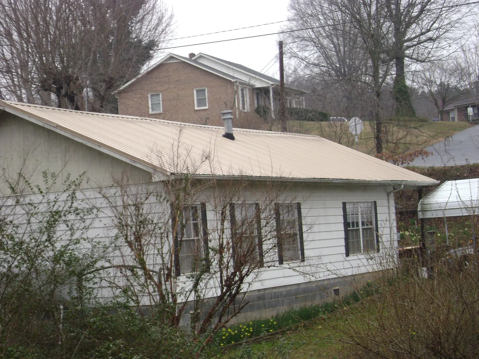 Tan metal roof on a white sided house set into a hillside — Commercial Roofing by Roofing Brothers in Fairplay