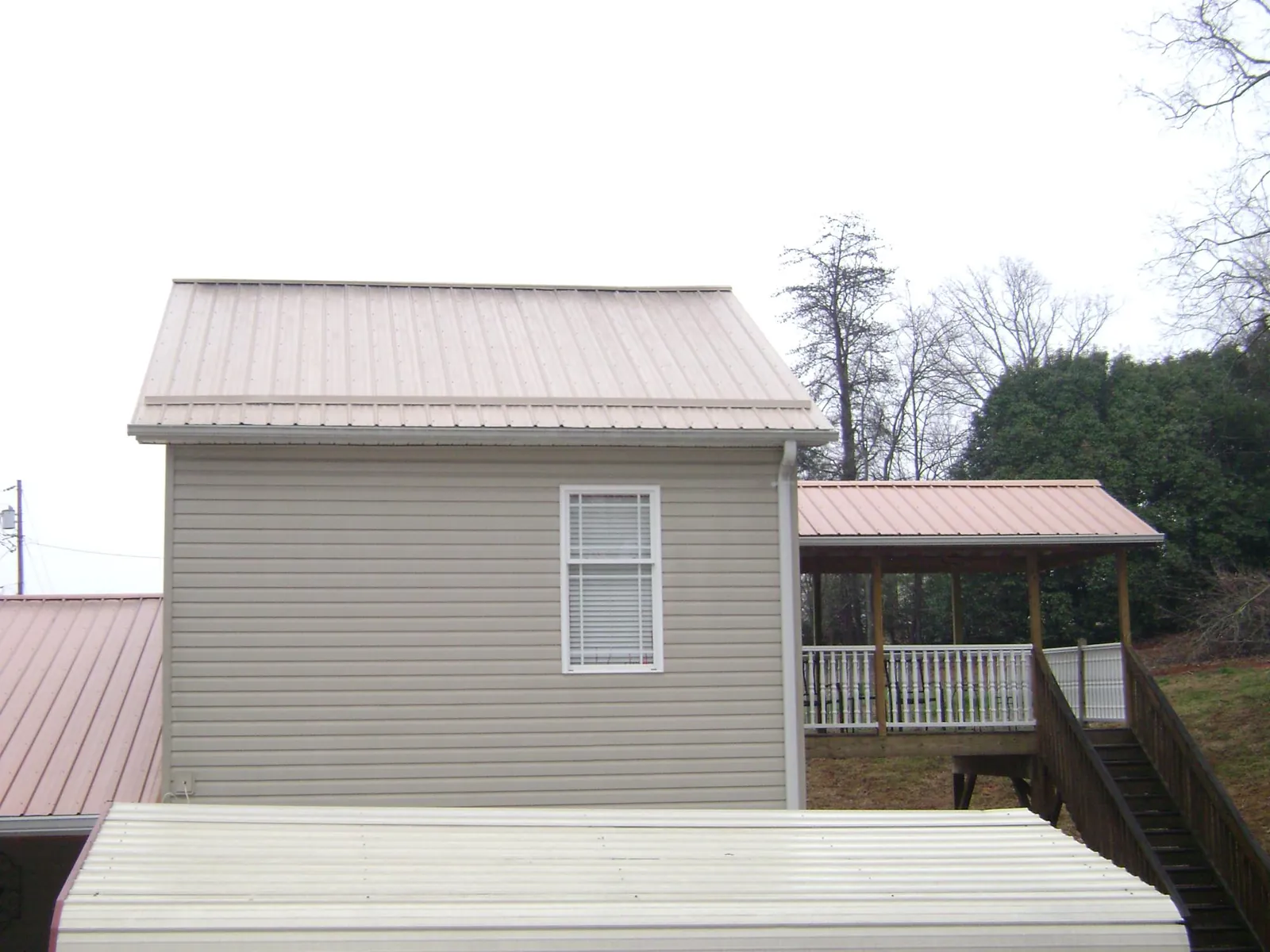 Tan metal roofs on a two story addition and attached porch, from a Roof Replacement job in Fairplay